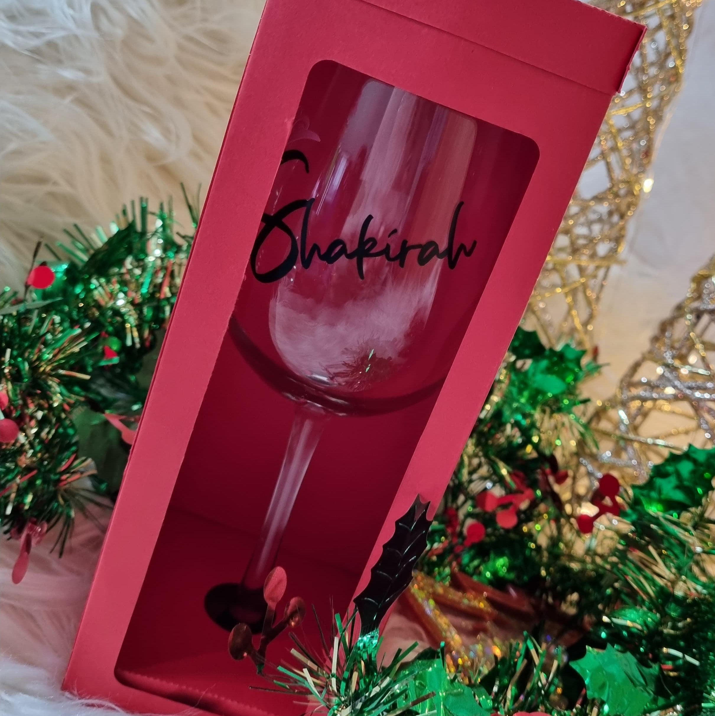 Red gift box with a wine glass inside, featuring the name 'Shakira', on a decorative background.